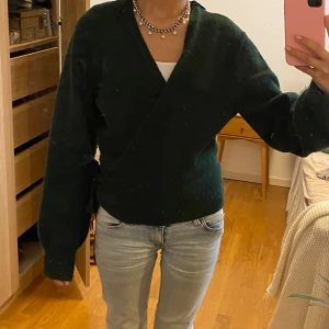 Grön omlottskofta ifrån & other stories - Säljer en jättefin mörkgrön stickad omlottskofta ifrån & other stories, koftan knyter man längs sidan av ena höften och är perfekt nu till vintern!! Går ej att köpa längre💕 Går gärna ner i pris vid snabb affär☺️