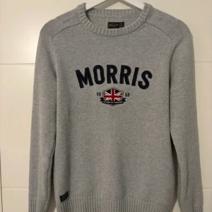 Grå stickad tröja från Morris - Snygg grå stickad tröja från Morris med broderad logga och brittisk flagga framtill. Tröjan har rund hals, ribbade muddar och lång ärm. Perfekt för dig som gillar klassisk stil med en modern twist.skriv vid minsta fråga 😁