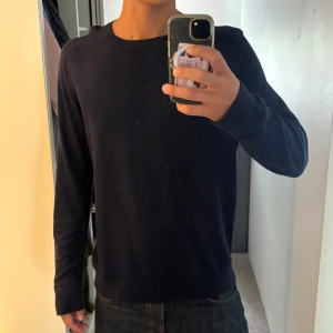 Mörkblå långärmad stickad tröja - En stilren mörkblå stickad tröja med rund halsringning och långa ärmar. Tröjan har en enkel och clean design utan synliga detaljer eller mönster, vilket gör den lätt att matcha med olika outfits. Perfekt för dig som gillar en klassisk look.