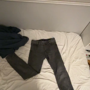 Grå slim jeans från Jack & Jones - Snygga grå jeans från Jack & Jones, modell Slim/Glenn. De har en smal passform och klassisk femficksdesign. Jeansen är tillverkade i ett stretchigt jeanstyg som sitter tajt men bekvämt. Perfekta för dig som gillar en stilren och modern look.