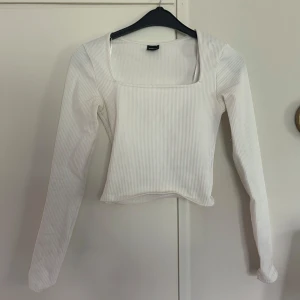 Vit ribbad topp från Gina Tricot - Säljer en stilren vit långärmad topp från Gina Tricot i ribbat material. Toppen har fyrkantig urringning och sitter snyggt figurnära. 