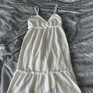 Vit sommarklänning från H&M Divided - Supersöt vit klänning från H&M Divided i storlek XS. Klänningen har smala axelband, v-ringad omlott upptill och ett rynkat midjeband som ger en flowy känsla. Materialet är lätt och strukturerat, perfekt för varma dagar. Passar dig som gillar enkel och fräsch stil. Använt den en gång!☺️ Som ny!