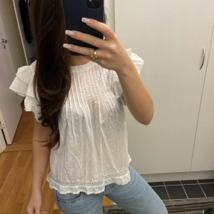 Vit blus med volangärmar - Söt vit blus med korta volangärmar, små prickar i tyget och fina spetsdetaljer längst ner. Storleken är 146-152 men passar mig som har S💕 Använts några få gånger. 