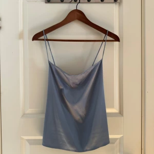 Ljusblå linnetopp med tunna axelband - Säljer en ljusblå linnetopp med tunna axelband och snygg draperad urringning. Toppen har en rak passform och är tillverkad i ett glansigt, silkesliknande material. Oanvänd prislapp kvar. 🩵