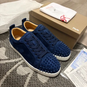 Blå Christian Louboutin sneakers med nitar - Snygga sneakers från Christian Louboutin i mörkblå mocka med matchande blå nitar på tån och klassisk röd sula. Skorna har rund tå, snörning och vit platt sula. Insidan är ljusbeige och de har en riktigt lyxig vibe. Perfekta för dig som vill sticka ut med exklusiva detaljer.