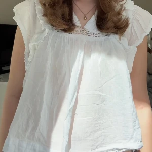 Vit volangblus med spetsdetalj - Säljer en luftig vit blus med volangkantade ärmar och v-ringning. Blusen har fina spetsdetaljer upptill och är tillverkad i ett tunt.