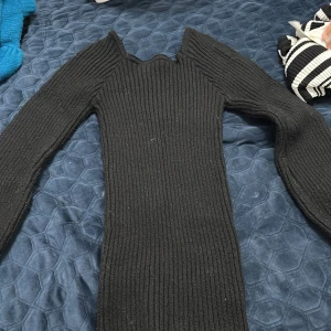 Svart ribbad klänning från SHEIN - Svart ribbad stickad klänning från SHEIN med lång ärm och figurnära passform. Klänningen har en unik kant vid halsen och är tillverkad i ett stretchigt material som sitter snyggt på kroppen. Perfekt för dig som gillar en stilren och edgy look.