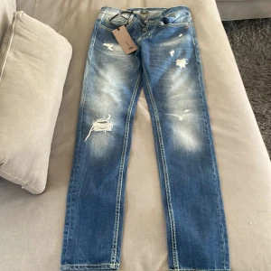 Blå slitna skinny jeans från Dondup - Snygga blå skinny jeans från Domdup med slitningar och distressed detaljer framtill. Jeansen har klassisk femficksdesign, ljusa partier och kontrastsömmar. Perfekta för dig som gillar en trendig och avslappnad look. Storlek 30