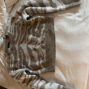 Beige och vit zebramönstrad tröja SHEIN - Supermysig stickad tröja från SHEIN i beige och vitt med zebramönster. Modellen är croppad med bred ribbad mudd i midjan och vid ärmslut. Perfekt för dig som vill ha en trendig och bekväm look till hösten eller vintern.