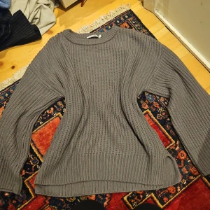 Grå stickad tröja från NA-KD - Säljer en grå stickad tröja från NA-KD i storlek M. Tröjan har en rund halsringning, ribbade muddar och långärmade ärmar. Perfekt för lager-på-lager och chill höst- eller vinterstil.