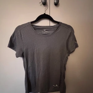 Grå träningst-shirt från Ronhill XS - Säljer en grå t-shirt från Ronhill i storlek XS. T-shirten har rund halsringning och korta ärmar, perfekt för träning. Tillverkad i ett lätt och snabbtorkande syntetmaterial som andas bra. Enkel och stilren design utan tryck eller mönster.