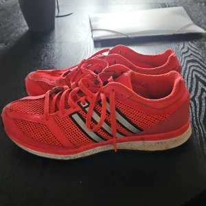Adidas träningsskor  - Säljer ett par Adidas sneakers med klassiska vita ränder på sidorna. Skorna har mesh-överdel för extra andningsförmåga, snörning och platt sula.