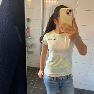 Pastellfärgad Champion t-shirt - Fräsch t-shirt från Champion med pastellfärgat tie-dye mönster i ljusblått, lila och grönt. Klassisk rund hals och korta ärmar. Champion-logga broderad på bröstet och ärmen. Skön bomullskvalitet och slim passform som sitter snyggt.