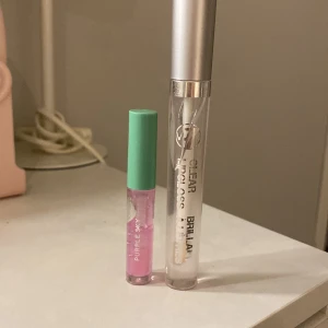 2-pack läppglans: Purple Sky & W7 Clear - Säljer två läppglans: ett från Purple Sky med mintgrönt lock och ljuslila glans, samt ett transparent läppglans från W7 med silverfärgat lock. Perfekta för glansiga läppar och enkel att ta med i väskan.