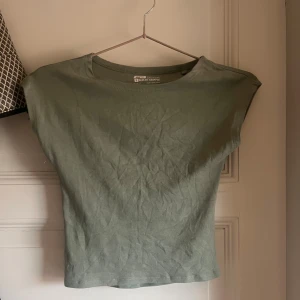 Grön croppad topp från FB Sister - Säljer en stilren grön croppad topp från FB Sister i slim fit-modell. Toppen är ärmlös med rund halsringning och tillverkad i mjuk bomull. Perfekt att matcha med höga jeans eller kjol för en enkel och snygg look.