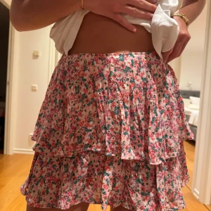 Blommig volangkjol från Zara - Supersöt kort volangkjol från Zara med blommigt mönster i rosa, grönt och vitt. Kjolen har flera lager volanger som ger en flowy känsla och är perfekt för varma dagar. 