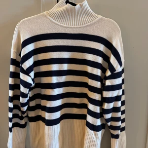 Randig polotröja i vitt och marinblått - Snygg och mjuk randig polotröja med breda marinblå och vita ränder. Tröjan har en ribbad polokrage och ribbade muddar vid ärmslut och nederkant. Tillverkad i en mjuk blandning av viskos, polyester och polyamid. 