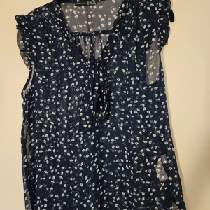 Blommig blus - Söt och luftig marinblå blus från Atmosphere med små vita blommor. Blusen är ärmlös med volangdetaljer på axlarna och har en v-ringning med knytband framtill. Storlek 40 men tycker snarare den passar S-M