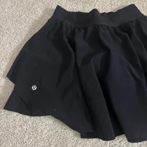 Lululemon kjol - Svart kortkjol från Lululemon med bred resår i midjan och flowig passform. Kjolen är tillverkad i polyesterblandning och har en sportig look, perfekt för träning eller tennis. Diskret Lululemon-logga på sidan och innerbyxa för extra komfort. Pris kan diskuteras vid snabbt köp💗