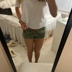 Olivgröna jeansshorts - Säljer ett par olivgröna, lågmidjade jeansshorts med råa kanter och slitna detaljer. Shortsen har knappgylf och klassiska fickor fram. Perfekta för varma dagar när du vill ha en avslappnad och cool stil.