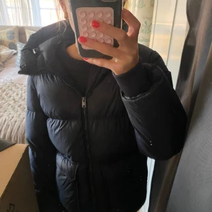 Mörkblå vinterjacka från Woolrich - Säljer en mörkblå dunjacka från Woolrich med huva och två stora fickor framtill. Jackan har en klassisk pufferstil, dragkedja hela vägen och diskret logga på ärmen. Perfekt för kalla dagar och riktigt skön att bära, perfekt vinter jacka