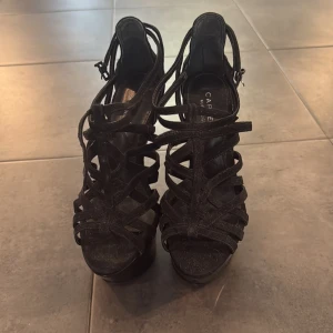 Svarta wedges från Carvela Kurt Geiger - Unika svarta wedges med 15cm hög klack från Carvela Kurt Geiger. Skorna har flera smala remmar i mocka, öppen tå och cool plattformssula utan häl. Perfekta för dig som vill sticka ut med en edgy och trendig look.