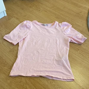 Ljusrosa topp från ONLY med puffärm - Säljer en söt ljusrosa topp från ONLY i storlek S. Toppen har puffiga korta ärmar och är gjord i mjuk bomull. Enkel och stilren design som passar perfekt till jeans eller kjol.