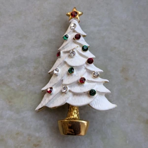 Julgransbrosch med strass och stjärna - Superfin brosch formad som en julgran i vitt med glittrande strass i rött, grönt och vitt. Toppen pryds av en guldfärgad stjärna och foten är också i guld. Perfekt accessoar för att sprida julkänsla!