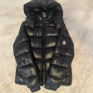 Svart Moncler dunjacka med huva - Svart glansig pufferjacka från Moncler i bra skick. Köptes från plick och använd en säsong