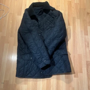 Svart quiltad jacka från Barbour L - Quiltad svart jacka från Barbour i storlek L. Klassisk modell med krage, tryckknappar och flera fickor framtill. Jackan har ett diskret Barbour-broderi på fickan och är fodrad för extra värme. Perfekt för kyliga dagar och snygg till alla outfits. Nypris runt 2500. Kom med prisförslag