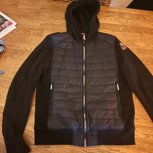 Svart quiltad jacka från Parajumpers - Snygg svart jacka från Parajumpers med quiltad front och ärmar i mjukt material. Jackan har huva, hel dragkedja och två fickor med dragkedja. Perfekt för dig som vill ha en stilren och sportig look med premiumkänsla. Är för både män och kvinnor för kvinnor är det s och män xs men passar även för s