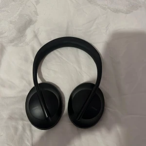 Bose Noise Cancelling Headphones 700 - Snygga svarta Bose 700 trådlösa over-ear hörlurar med aktiv brusreducering. Hörlurarna är i fint skick utan synliga repor eller skador. Perfekt för musik, resor och arbete tack vare lång batteritid och bekväm passform.