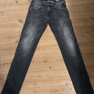 Replay Anbass svarta jeans, stl 30 - Säljer ett par Replay Anbass jeans i svart tvätt med snygga slitningar. Jeansen har klassisk femficksdesign, smal passform och raka ben. Materialet är stretchigt jeans för extra komfort. Perfekta för dig som gillar en modern och stilren look.