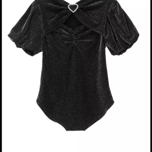 Glittrig svart topp med hjärtformad detalj - Supersnygg svart glittrig topp med puffärmar och en hjärtformad strassdetalj vid halsen. Toppen har en cut-out framtill och är figurnära med korta ärmar. Perfekt för dig som vill sticka ut med en glamorös vibe.