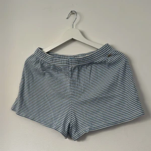 Randiga blåvita shorts från Pull&Bear - Snygga shorts från Pull&Bear i Pacific Republic-kollektionen, med blå och vita smala ränder. Modellen har elastisk midja och är tillverkad i mjuk bomull med lite elastan för extra komfort. Perfekta för chill dagar och sommarhäng.