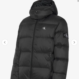 Svart pufferjacka från Calvin Klein - Säljer en svart pufferjacka från Calvin Klein med huva och dragkedja. Jackan har CK-logga på bröstet och ärmen, samt två fickor med dragkedja. Perfekt för kalla dagar och riktigt snygg streetstil. Hör av dig vid intresse eller frågor.