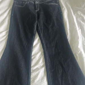 Mörkblå bootcut jeans med kontrastsömmar - Snygga mörkblå jeans med bootcut passform och tydliga vita kontrastsömmar. Klassisk femficksmodell med normal midja och dragkedja. Perfekta för dig som gillar en retroinspirerad look och vill ha ett par jeans som sticker ut lite extra.
