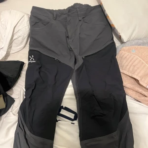 Svarta och grå friluftsbyxor Haglöfs - Säljer ett par svarta och grå friluftsbyxor från Haglöfs med dragkedjor vid knäna och flera fickor. Perfekta för utomhusaktiviteter och har en bekväm passform med elastisk midja. Slitstarka och funktionella för äventyr.