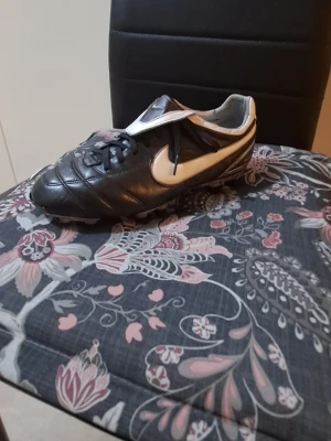 Nike svartvita fotbollsskor i skinn - Säljer ett par klassiska nike tiempo svartvita fotbollsskor med snörning och rund tå. Skorna har en vit Nike-swoosh på sidan, svart ovandel i skinn och dobbar som har bra grepp på gräsmattan skorna är stabila.                                                  Inte fasta priser