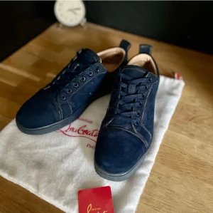 Mörkblå sneakers från Christian Louboutin - Snygga mörkblå sneakers från Christian Louboutin i mjuk mocka med rund tå och platt sula. Skorna har snörning och diskret broderad logga på hälen. Insidan är ljusbeige och de kommer med originalpåse och äkthetskort. Perfekta för dig som gillar exklusiv streetstyle.