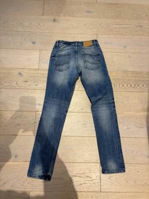 Jack & Jones Tim Slim Fit Jeans w32 l34  - Säljer ett par blå Jack & Jones Tim Slim Fit jeans med klassisk femficksdesign och snygga slitningar. Jeansen har normal midja och raka ben med en smal passform. Tillverkade i slitstarkt denim av bomull. W32 34l. Skickar jeans dagen efter köpet 
