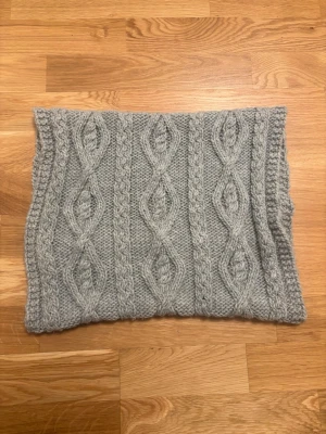 Grå stickad halsvärmare från H&M - Säljer en grå stickad halsvärmare från H&M med snyggt flätmönster. Den är mjuk och chunky, perfekt för att hålla dig varm under kyliga dagar. Passar dig som gillar enkel men stilren design och vill ha något som känns cozy och trendigt.