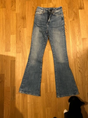 Blå Peachy Flare jeans, waist S, längd 31 - Snygga blå Peachy Flare jeans från Never Denim med klassisk femficksdesign och dragkedja. Modellen har hög midja och riktigt utsvängda ben. 