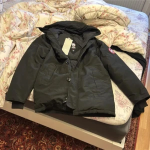 Canada Goose - Canada Goose dunjacka i svart med huva och klassisk logga på ärmen. Jackan har både dragkedja och knappar framtill, två stora fickor och en clean, stilren look. Perfekt för kalla dagar och har en schysst oversized passform. Priset går att diskutera som allt annat på min profil 👍😊