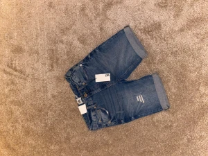 Blå jeansshorts från 157 - Snygga blå jeansshorts från 157 med klassisk femficksdesign, uppvikta benslut och slitna detaljer framtill. Shortsen har normal passform och är tillverkade i bomull för en skön känsla. Perfekta för varma dagar när du vill ha en avslappnad look.