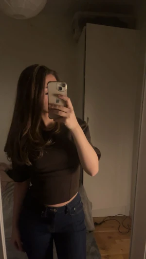 Brun croppad topp från Gina Tricot - Säljer en stilren brun croppad topp från Gina Tricot med rund hals och korta ärmar. Toppen har en clean look och är tillverkad i ett mjukt material som sitter snyggt på kroppen. Perfekt att matcha med jeans eller kjol för en trendig vibe.