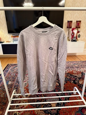 J. Lindberg sweatshirt  - Säljer en stilren grå sweatshirt från J.Lindeberg i storlek XL. Tröjan har rund hals, lång ärm och en svartvit broderad logga på bröstet. Tillverkad i mjuk bomull för en skön och avslappnad känsla. Vid minsta funderingar så är det bara att höra av sig mvh CH