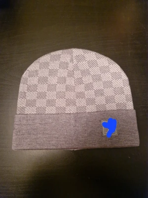 Lyxig grå mössa - Snygg grå mössa med rutigt mönster och bred uppvikt kant. Perfekt för dig som gillar stilrena accessoarer med lite edge. Mössan är stickad i mjukt material som håller dig varm.