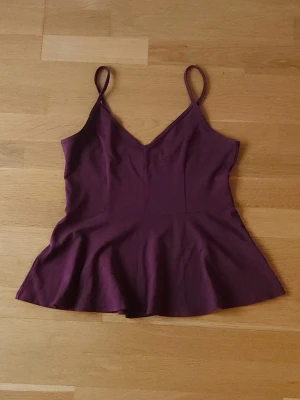 Vinröd topp - Vinröd topp med smala axelband och v-ringad hals. Toppen har en lätt utsvängd nederdel som ger en snygg siluett. Enkel och stilren design som är lätt att matcha. 