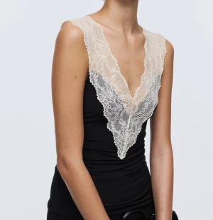 Svart linnetopp med spetsdetaljer - Slutsåld fin topp från H&M. Säljer en svart linnetopp med breda axelband och djup v-ringning, dekorerad med krämvit spets framtill och längs axelpartiet. Säljer då jag beställde fel storlek. 